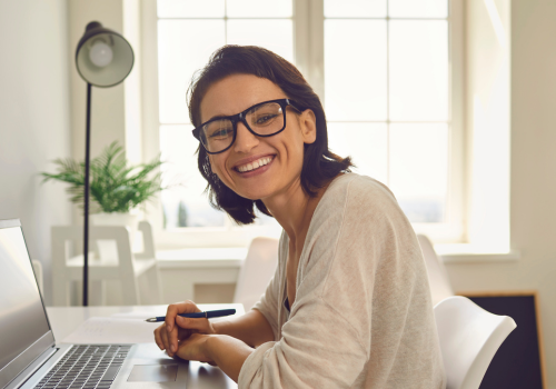 A woman with glasses and brown hair smiling and working from home