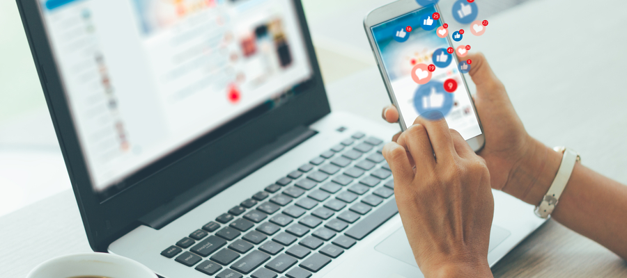 Phone and a laptop with symbols of social media icons floating from the phone