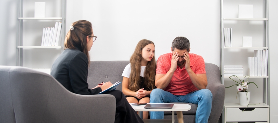 A social worker with a man struggling with his head in his hands, next to a young girl