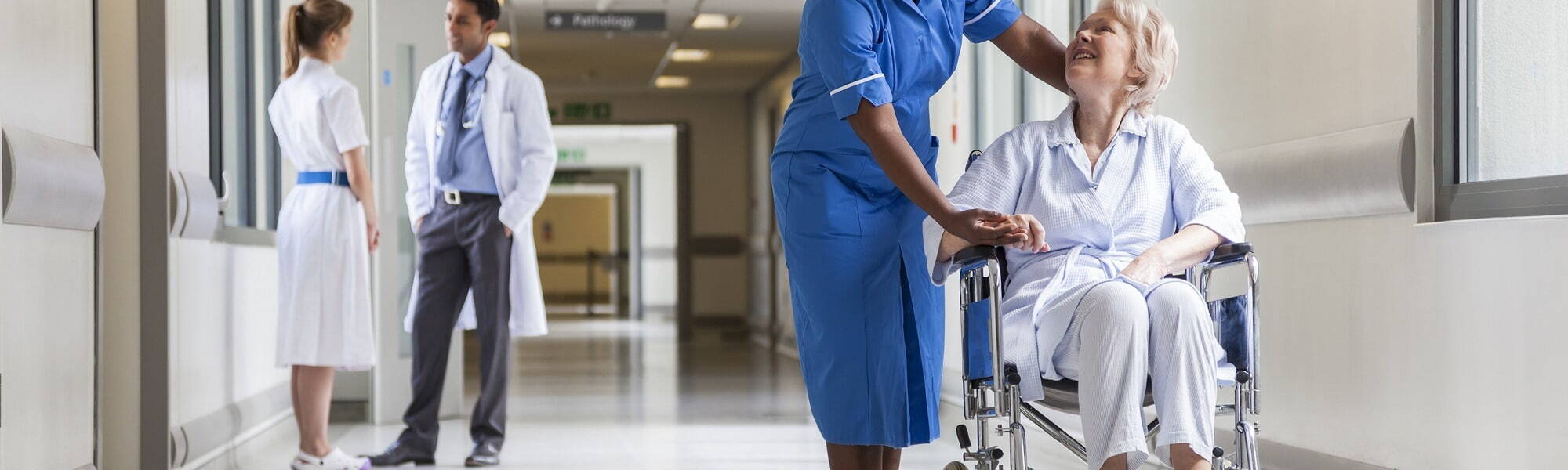 Hospital setting showing a patient in a wheelchair, and a doctor having a conversation in the background